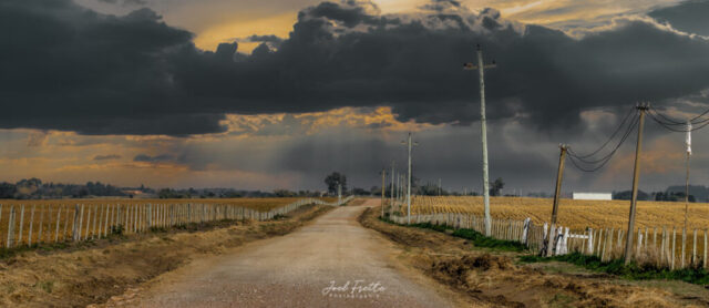 Chemin de terre rural bordé de clôtures et de poteaux électriques sous un ciel dramatique chargé de gros nuages d'orage sombres